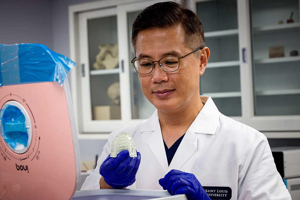 Dr. Kim wears a white lab coat, blue gloves and holds a 3D-printed aligner.