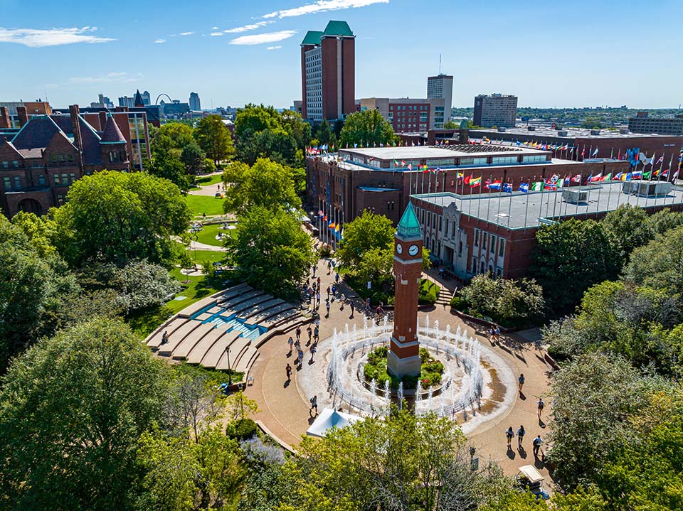 Aerial view of people walking around the clock tower on the SLU campus with historic buildings and lush green trees.
